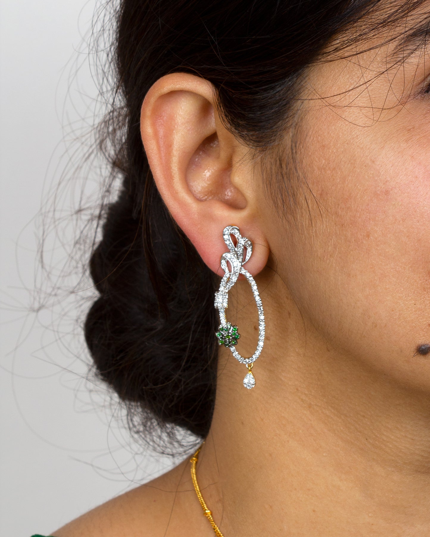 Bindhani gold-plated with matching earrings, white stone studded abstract swirl design, green crystal flower accents, and drop detailing for ethnic party wear.