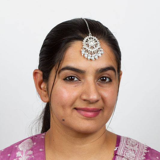 Model wearing Bindhani silver-plated round small tikka for women, featuring a pearl drop and delicate stone detailing on the forehead.