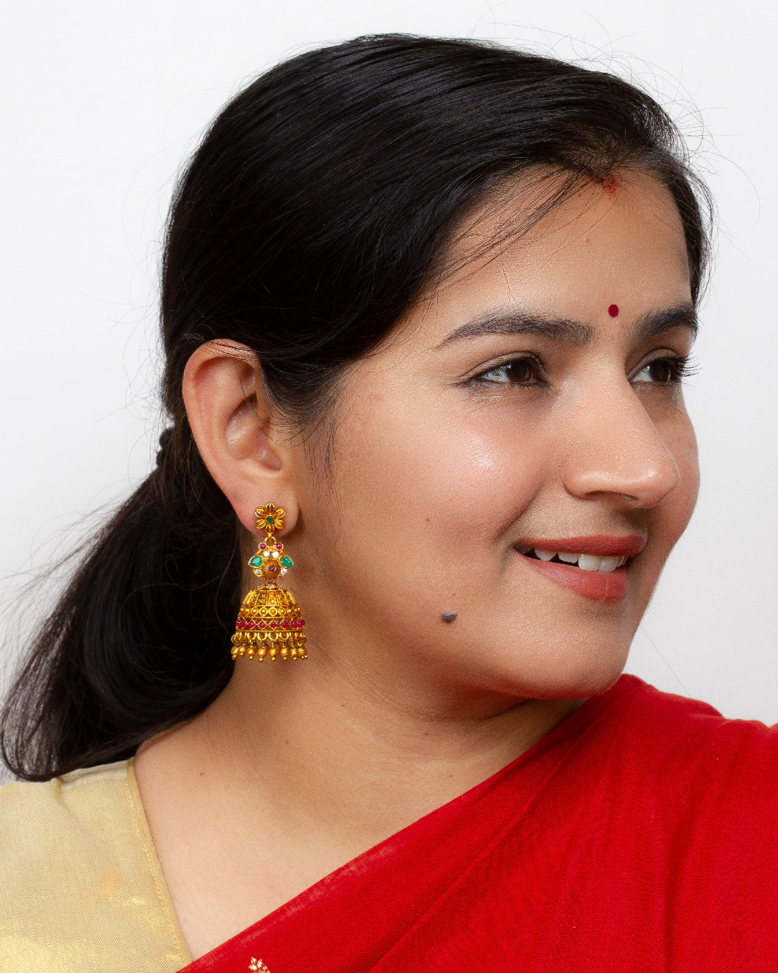 Bindhani model wearing south indian jhumka with ruby green stones and golden beads drops for women in red sarees