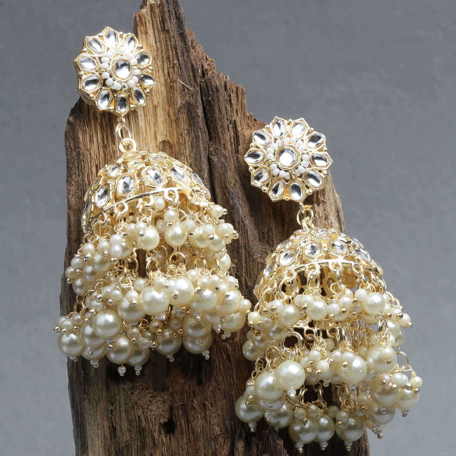 Bindhani gold plated jhumka earrings with white hanging pearls and kundan stone kept on wood piece 