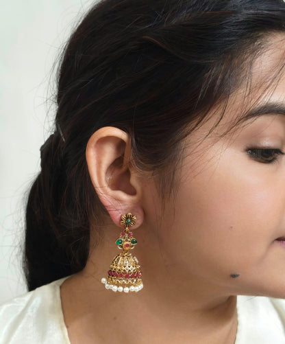 Bindhani antique gold-plated jhumka earrings featuring an intricately embossed dome design with a floral motif and a round green pink stone stud. 
The traditional temple-style earrings are adorned with engraved gold bead danglers, creating an elegant ethnic look. Lightweight drop earrings with a secure push-back closure, displayed on a white background. Perfect for weddings, festive occasions, cultural events, and traditional wear.