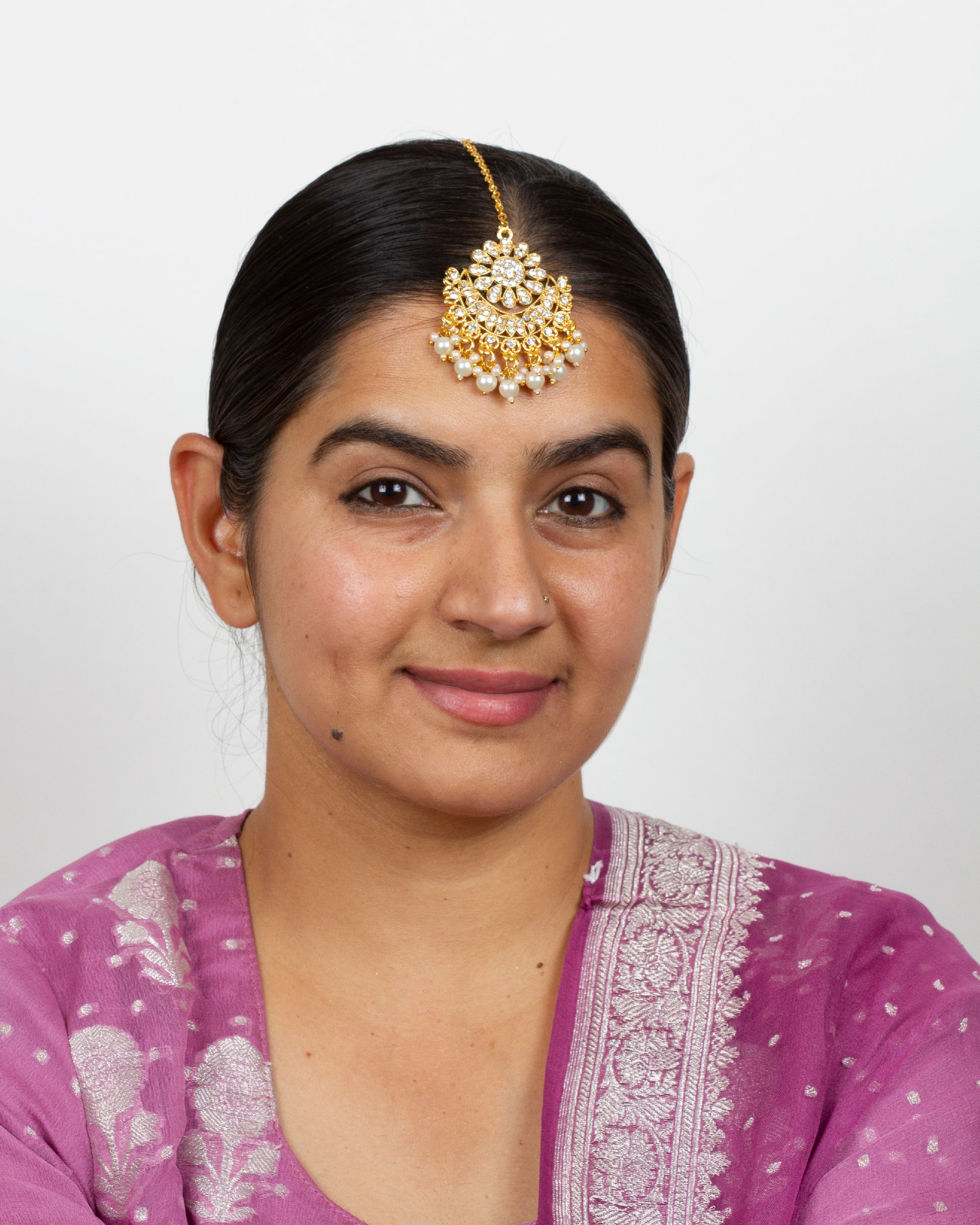Model wearing Bindhani gold-plated round small tikka for women, featuring a pearl drop and delicate stone detailing on the forehead.