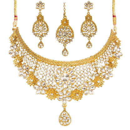 Bindhani gold-plated choker necklace set featuring white Kundan stones, floral motifs, intricate lattice detailing, crystal accents, and a teardrop pendant. The set includes matching floral drop earrings and a coordinating maang tikka with teardrop danglers, displayed on a white background.