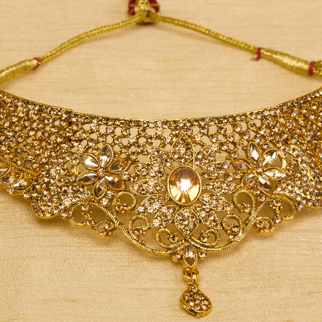 Front view Bindhani gold-plated bridal necklace set for women featuring an intricate floral filigree choker design with sparkling stone embellishments,on a grey background.