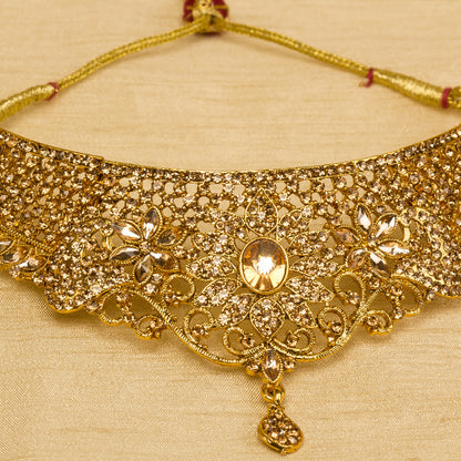 Front view Bindhani gold-plated bridal necklace set for women featuring an intricate floral filigree choker design with sparkling stone embellishments,on a grey background.
