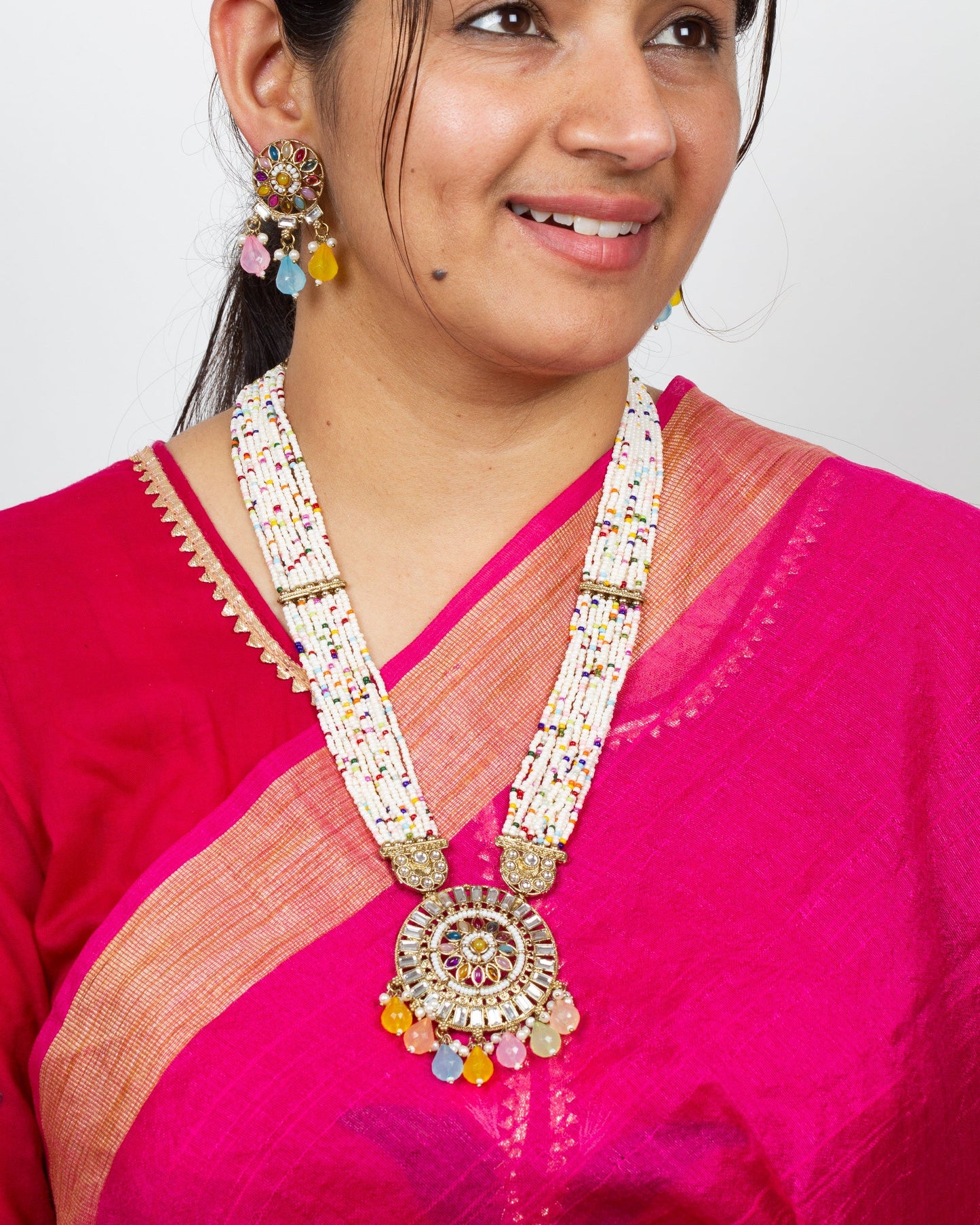 Woman wearing a Bindhani long Kundan stones Rani Haar pendant necklace set featuring intricate antique gold-plated craftsmanship with sparkling Kundan stones, traditional royal-inspired long necklace design, matching pendant, and coordinated earrings. Elegant ethnic jewelry set ideal for weddings, festive occasions, and bridal wear.