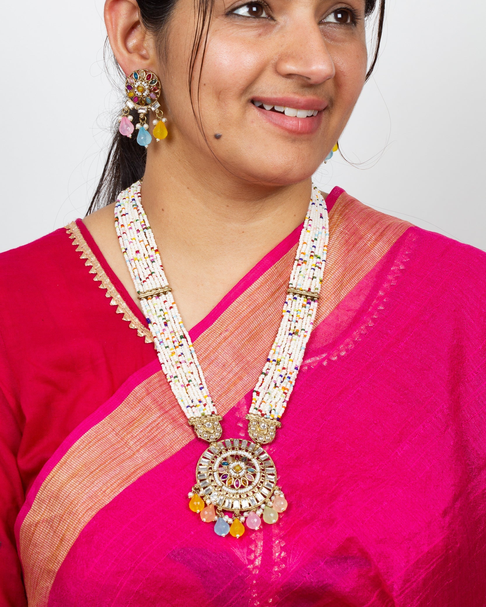 Woman wearing a Bindhani long Kundan stones Rani Haar pendant necklace set featuring intricate antique gold-plated craftsmanship with sparkling Kundan stones, traditional royal-inspired long necklace design, matching pendant, and coordinated earrings. Elegant ethnic jewelry set ideal for weddings, festive occasions, and bridal wear.