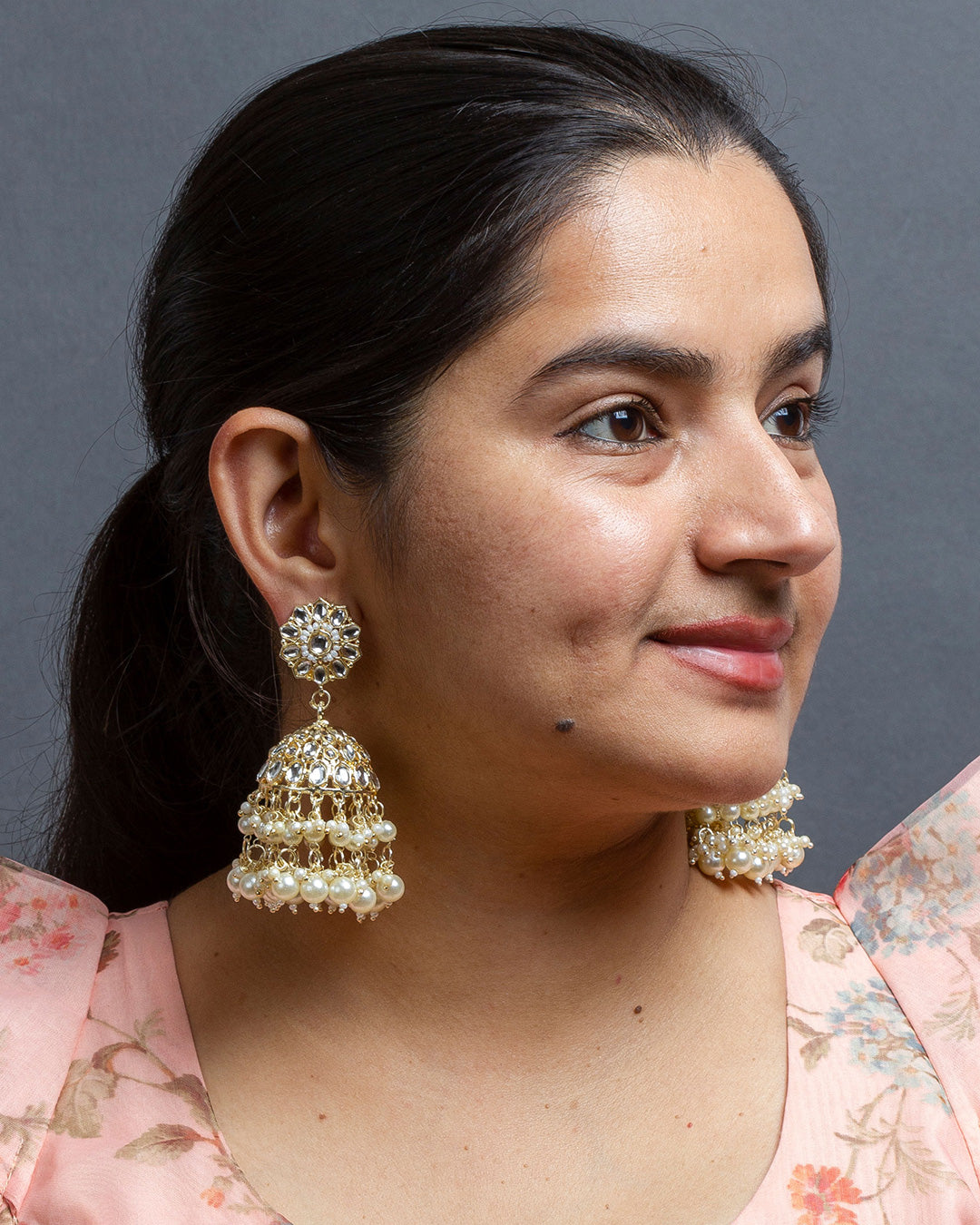 Model wearing handcrafted gold-toned kundan-work jhumka earrings with white bead drops,