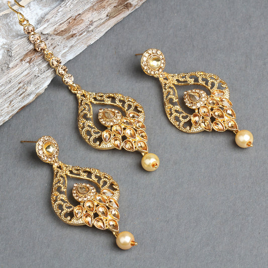 Bindhani gold-plated earrings and maang tikka set featuring leaf-shaped openwork designs with intricate filigree detailing, floral motifs, and sparkling crystal stone embellishments. The matching earrings and tikka are finished with elegant cream pearl drops, creating a traditional bridal jewelry look. Displayed on a grey background with a crystal-studded maang tikka chain visible.