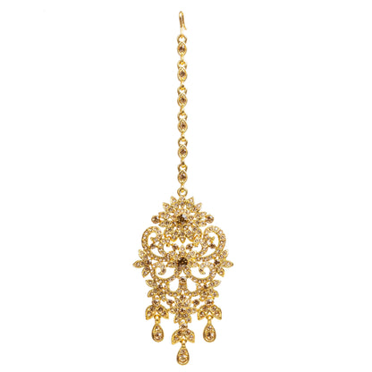 Bindhani gold-plated maang tikka featuring champagne-colored LCT stones with sparkling crystal accents. The tikka showcases an intricate floral and scrollwork design with detailed openwork filigree, a central stone motif, and three dangling teardrop-shaped LCT stone drops. Front view displayed on a white background.