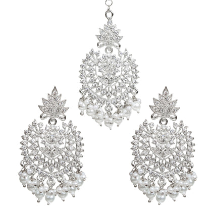 Bindhani silver-plated jewelry set featuring a matching maang tikka and statement earrings. The earrings showcase a leaf-shaped stud top, intricate openwork floral and geometric design embellished with clear stones, a central round stone, and white pearl bead tassels. The coordinating maang tikka features the same leaf and floral motif with dangling white pearl bead clusters. Front view displayed on a white background.