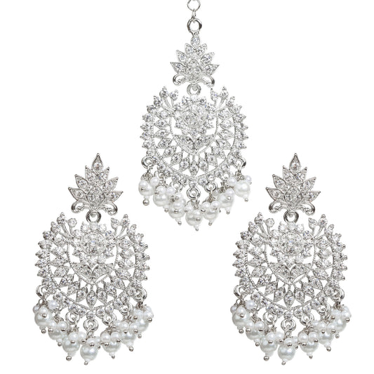 Bindhani silver-plated jewelry set featuring a matching maang tikka and statement earrings. The earrings showcase a leaf-shaped stud top, intricate openwork floral and geometric design embellished with clear stones, a central round stone, and white pearl bead tassels. The coordinating maang tikka features the same leaf and floral motif with dangling white pearl bead clusters. Front view displayed on a white background.