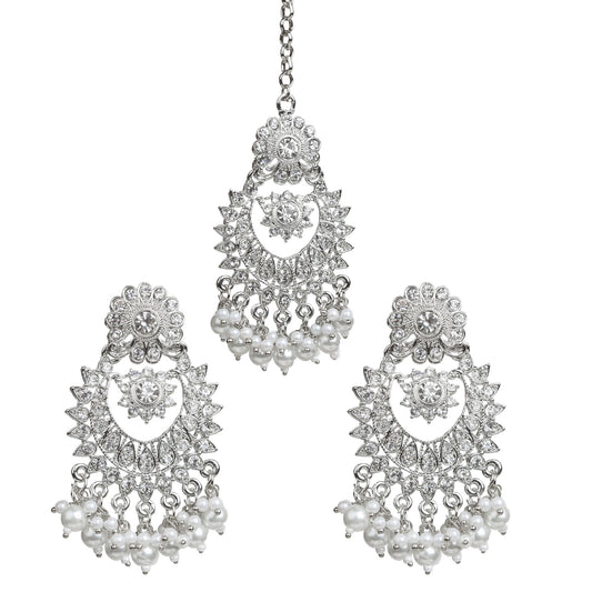 Bindhani silver-plated earrings tikka set featuring a matching maang tikka and chandbali earrings. The earrings showcase intricate floral and crescent-shaped designs embellished with clear stones, an ornate floral centerpiece, and white pearl bead tassels. The coordinating maang tikka stone the same elegant design with pearl bead drops. Front view displayed on a white background.
