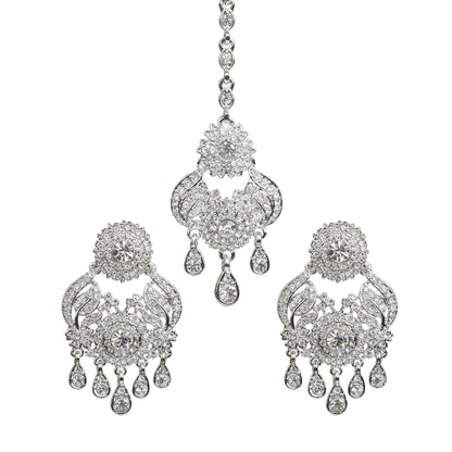 Bindhani silver-plated jewelry set featuring a matching maang tikka and statement earrings. The earrings showcase a circular floral stud top, intricate openwork design embellished with clear stones, a central round stone, curved decorative detailing, and multiple teardrop stone danglers. The coordinating maang tikka features a floral and paisley-inspired design with clear stone detailing and matching teardrop drops. Front view displayed on a white background.