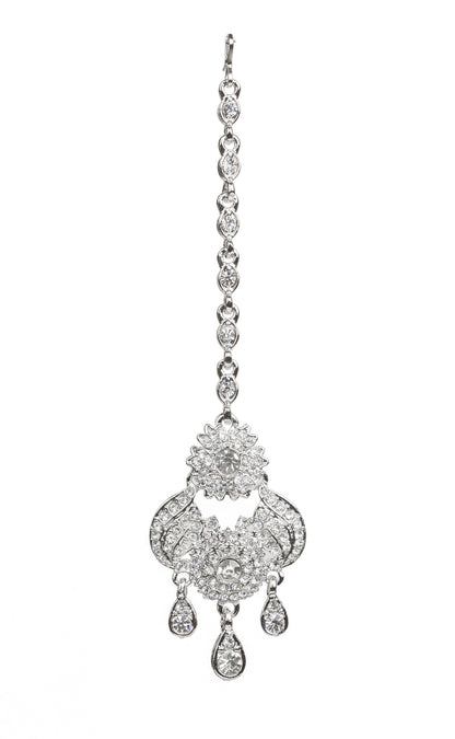 Bindhani silver-plated maang tikka featuring an intricate floral and paisley-inspired design embellished with clear stones. The tikka showcases a central floral motif, curved decorative detailing, and multiple teardrop-shaped stone danglers. Attached to a delicate silver-toned chain. Front view displayed on a white background.