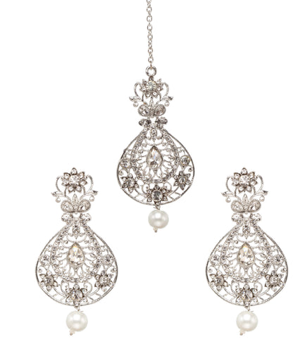Bindhani silver-toned maang tikka and earrings set featuring clear stones with intricate floral and teardrop-shaped detailing and white pearl drop accents. The maang tikka showcases an elegant teardrop design with stone-studded openwork patterns and a single pearl drop, while the matching earrings feature floral tops, teardrop-shaped stone designs, and pearl hanging drops. Front view displayed on a white background.