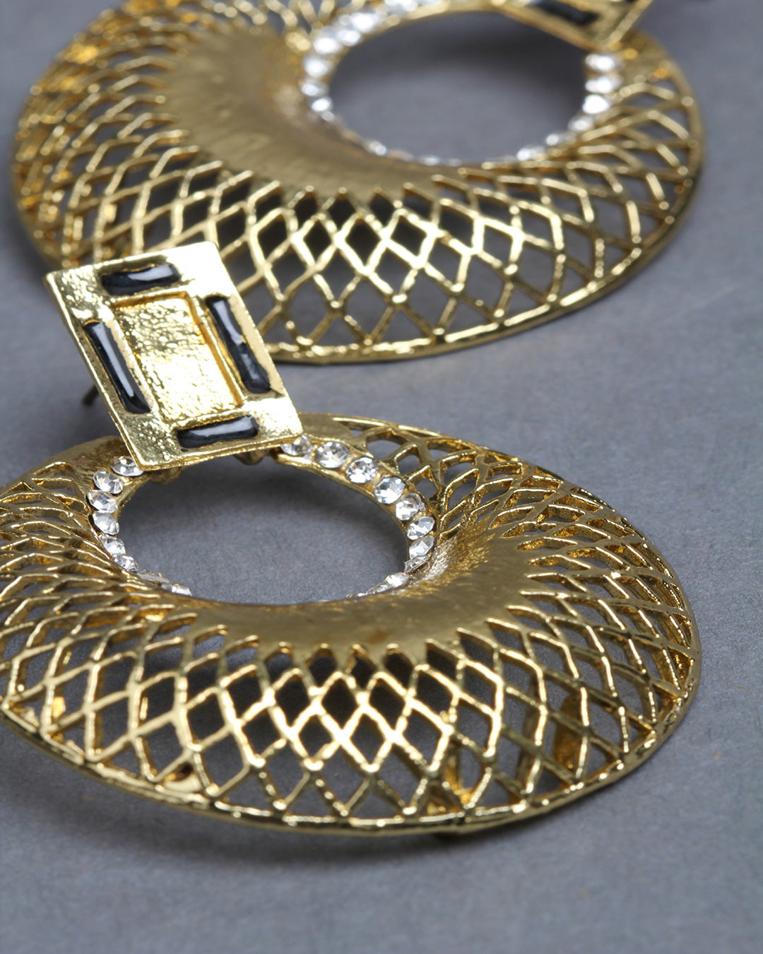 Close-up zoom view of Bindhani gold-plated geometric earrings, highlighting the intricate lattice cutwork pattern on the circular hoop, textured gold finish, rectangular stud top, and delicate white stone detailing around the inner ring. The detailed craftsmanship and polished traditional design are clearly visible.